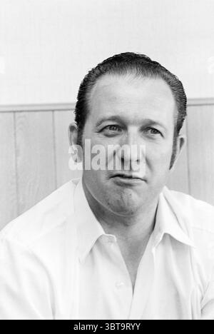 Portrait of Mr. Pike Portraits, Whizgle News, Dutch Desk, The Netherlands, 1950 - 2000 on 11-05-1970. The image shows these topics. The scene features a middle-aged man with slicked-back hair, demonstrating a tidy and deliberate style. He is wearing a light-colored shirt, which is buttoned up and neatly pressed. The fabric appears smooth, reflecting a sense of care in his appearance. His expression seems contemplative and serious, with slight furrows on his brow, suggesting deep thought or contemplation. The man is sitting against a backdrop of light-colored walls that create an airy and neutr Stock Photo