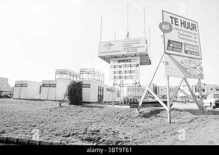 Exterior information center Velserbroek, Whizgle News, Dutch Desk, The Netherlands, 1950 - 2000 on 10-03-1994. The image shows these topics. The scene showcases a semi-urban area with a focus on various architectural structures. In the foreground, a large, elevated sign stands prominently, supported by a sturdy framework. The sign features a combination of rectangular panels, suggesting it may serve as an informational hub or advertisement for nearby developments, indicated by the words and numbers visible. Surrounding the sign, there are several low-rise buildings, likely commercial, with lar Stock Photo