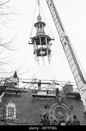 Placing a new tower on Heemstede Town Hall Town Halls Tower Heemstede The Netherlands, Whizgle News, Dutch Desk, The Netherlands, 1950 - 2000 on 21-04-1988. The image shows these topics. The scene captures a moment of architectural renovation, set against a somber, overcast sky that casts a muted gray light over the entire area. In the foreground, a tall crane dominates the composition, its metallic arm extended outward, holding aloft a delicate structure resembling a cupola, adorned with intricate details and a pointed spire at the top. The cupola is crafted with a blend of materials, showcas Stock Photo