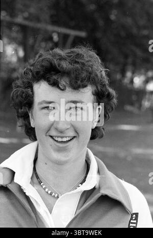 Portraits Bloemendaal hockey (women) Portraits, Whizgle News, Dutch Desk, The Netherlands, 1950 - 2000 on 16-09-1979. The image shows these topics. In the scene, a person is depicted with a bright and engaging smile, displaying a sense of warmth and approachability. Their hair is dark and curly, framing their face and adding to a youthful appearance. The individual wears a collared shirt, suggesting a casual yet put-together style, with the collar slightly upturned. Around their neck, a simple necklace adds a subtle touch of detail. The background is softly blurred, featuring gentle hints of g Stock Photo