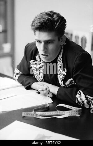 Fashion designer Vincent Blom Haarlem The Netherlands, Whizgle News, Dutch Desk, The Netherlands, 1950 - 2000 on 22-01-1995. These are the elements in the image. In a monochrome scene, a young man sits at a table, visibly engrossed in thought. His hair is styled in a sharp, slightly messy manner, emphasizing the intensity of his expression. He is dressed in a striking garment featuring a bold, zebra-like pattern, contrasting with the solid black of the rest of his outfit. The table is cluttered with various pieces of fabric and paper, hinting at a creative endeavor, possibly related to fashion Stock Photo