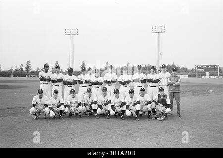 Dutch baseball team Baseball characters, Whizgle News, Dutch Desk, The Netherlands, 1950 - 2000 on 18-06-1969. The image includes these topics. The scene captures a group of individuals posed together on a grassy field, likely a baseball diamond. In the foreground, there are several players dressed in matching uniforms, predominantly white with dark accents, which may indicate a team identity. The players are standing in two rows; the back row features taller individuals, some displaying confident stances, while the front row features others crouching or seated. The uniforms reveal a sense of Stock Photo