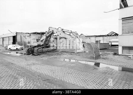 CBS interiors + exteriors back in business Grammophone and record companies, Whizgle News, Dutch Desk, The Netherlands, 1950 - 2000 on 06-10-1980. These are the topics in the image. The scene features a construction site characterized by a stark, industrial atmosphere. In the foreground, a large excavator stands prominently, its mechanical arm bent as if preparing to scoop up debris. The excavator's metallic surface is a blend of muted greys and whites, reflecting a slightly worn exterior that suggests frequent use. The ground is a mix of dirt and asphalt, marked with puddles that catch reflec Stock Photo
