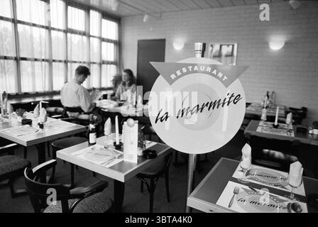 Restaurant Bastion hotel in Hoofddorp Hoofddorp Adrianahoeve The Netherlands, Whizgle News, Dutch Desk, The Netherlands, 1950 - 2000 on 24-06-1992. The image contains these topics. The scene captures an indoor dining area of a restaurant, characterized by a clean and modern aesthetic. The walls are a muted tone, likely beige or light gray, enhancing the bright ambiance provided by large windows that allow natural light to flood the space. Tables are arranged neatly throughout, set with white tableware, including plates and folded napkins, suggesting a careful attention to detail in the dining Stock Photo