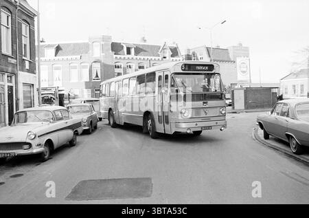 NZH bus line 5 on the corner Nagtzaamstraat - Teding van Berkhoutstraat Haarlem Nagtzaamstraat The Netherlands., Whizgle News, Dutch Desk, The Netherlands, 1950 - 2000. The image shows these topics. The scene depicts a bustling urban intersection characterized by a mix of vintage automobiles and a prominently featured bus. The bus, large and slightly boxy in shape, is painted in muted shades of gray and white, drawing attention with its significant size and the number indicating its route displayed prominently at the front. It is turning sharply, maneuvering through the narrow street, showcasi Stock Photo