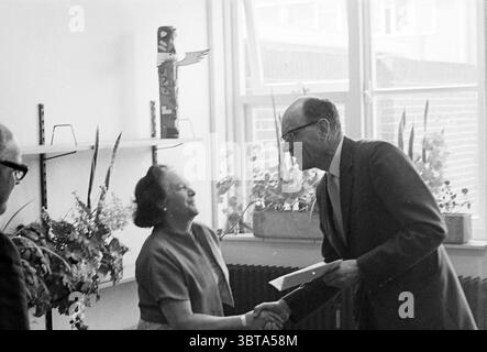 Anniversary Mr. La Blance gem. library IJmuiden Jubilee anniversaries, Whizgle News, Dutch Desk, The Netherlands, 1950 - 2000 on 21-04-1971. The image contains these topics. The scene captures a moment of interaction between two individuals. A woman, dressed in a simple yet elegant top, exudes warmth as she smiles and extends her hand in greeting. Her hair is styled neatly, framing her face, while her body language conveys openness and positivity. The man before her, wearing glasses and a formal suit, shares a smile, his expression suggesting approval or friendliness. He is also reaching out, Stock Photo