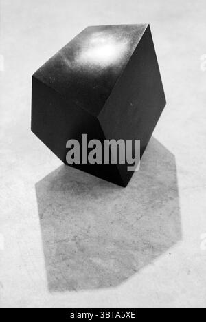 Sculpture gallery Rumpf Haarlem The Netherlands, Whizgle News, Dutch Desk, The Netherlands, 1950 - 2000 on 25-11-1992. The image contains these topics. The scene features a striking black polyhedral object, characterized by its angular edges and geometric shapes. The surface of the object is smooth and glossy, reflecting light in a way that creates a subtle sheen, emphasizing its three-dimensional form. The backdrop appears to be a textured, light-colored surface, perhaps a soft gray or beige, which contrasts sharply with the deep black of the polyhedron. This contrast draws the eye to the obj Stock Photo