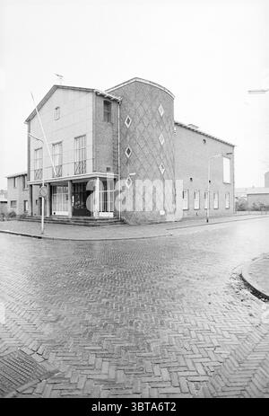 Exterior Reformed Youth Building IJm. Exterior, Whizgle News, Dutch Desk, The Netherlands, 1950 - 2000 on 29-11-1977. These topics appear in the image. The scene presents a striking architectural structure characterized by its unique design elements. The building features a blend of geometric shapes; one section is rectangular, while another presents a rounded, vertically oriented form. The exterior showcases a combination of smooth and textured surfaces, highlighted by a series of diamond patterns that adorn the curved side. The color palette remains understated, primarily comprised of muted Stock Photo