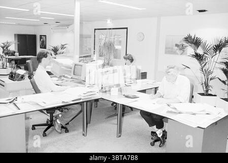 Printing company Planeta., Whizgle News, Dutch Desk, The Netherlands, 1950 - 2000 on 19-08-1992. These topics appear in the image. The scene depicts an office environment characterized by a blend of professionalism and casual engagement. In the foreground, three individuals are positioned around a large, multi-faceted desk. The desk is cluttered with papers, folders, and office supplies, creating a sense of busyness and productivity. To the left, a man is seated in a swivel chair, intently focused on a computer monitor. He wears a light-colored shirt and displays an engaged posture. His desk a Stock Photo