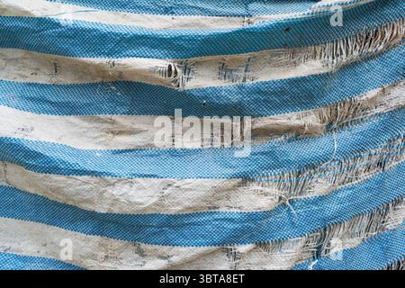 An old, tattered blue construction site tarpaulin Stock Photo