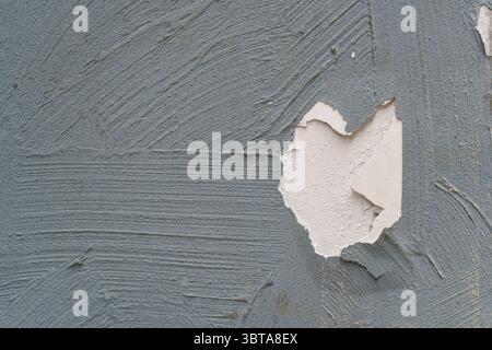 A wall with thick gray paint, featuring a cracked hole that reveals the white wall underneath Stock Photo