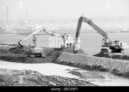 Activities Averijhaven IJm IJmuiden The Netherlands, Whizgle News, Dutch Desk, The Netherlands, 1950 - 2000 on 06-03-1991. The image contains these topics. The scene depicts a coastal area with a prominent industrial backdrop. Several large construction machines are actively working near the water’s edge, with two prominent excavators extending their arms towards heaps of earth and gravel. The excavators are painted in a stark contrast of yellow and gray, adding a bold visual element against the more muted tones of the surroundings. The ground is uneven, layered with piles of dirt and debris, Stock Photo