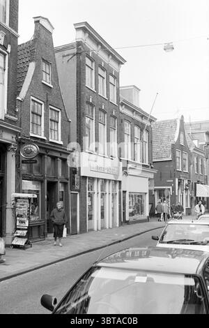 Exterior Kruisweg 31 + 37 Haarlem Kruisweg The Netherlands, Whizgle News, Dutch Desk, The Netherlands, 1950 - 2000 on 13-03-1991. The image contains these topics. The scene features a narrow, cobbled street lined with buildings characterized by traditional architecture, showcasing steep, gabled roofs. The façade of the buildings presents a mix of dark brick and light-colored plaster, creating a contrast against the sky. Some structures exhibit decorative elements such as ornate window frames and shutters. On one side of the street, a café or small shop displays an inviting entrance, complete w Stock Photo