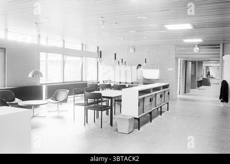 Interior Design Vogelenzang Interior, Whizgle News, Dutch Desk, The Netherlands, 1950 - 2000 on 12-09-1967. The image includes these topics. The scene features a spacious, modern interior that emphasizes minimalism and functionality. The color palette is predominantly monochromatic, with a blend of grays and blacks that gives a clean and serene appearance. Natural light floods through large windows, casting soft shadows across the open space, enhancing the tranquil atmosphere. To the left, there are a few circular chairs with sleek designs, arranged around a low coffee table. The furniture has Stock Photo