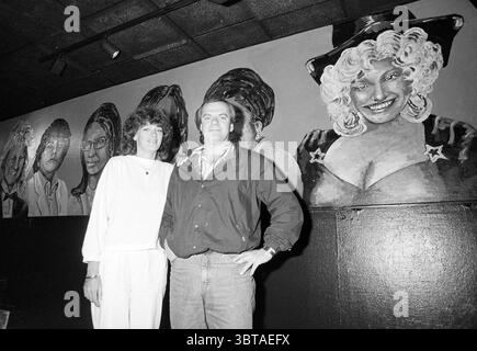 Man and woman in front of a mural by artists including Nana Mouskouri Lee Towers Michael Jackson André Hazes, Whizgle News, Dutch Desk, The Netherlands, 1950 - 2000 on 07-1988. These topics appear in the image. The scene captures a lively interior, likely a venue dedicated to music or entertainment. The backdrop features a large mural depicting several portraits of notable figures, each characterized by distinct hairstyles and expressions. The colors of the mural vary, showcasing a mix of shades that emphasize the personalities portrayed, predominantly featuring blacks, whites, and skin tones. Stock Photo