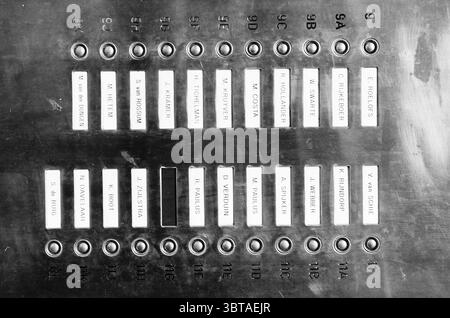 Miscellaneous nameplates, Whizgle News, Dutch Desk, The Netherlands, 1950 - 2000 on 26-02-1996. The image includes these topics. The scene features a metallic panel filled with a grid of small rectangular labels, each containing a name. The surface has a slight sheen, reflecting light in a way that emphasizes its industrial feel. The labels are primarily white against the dark metal, which creates a stark contrast. The arrangement of the labels is organized into several columns, each featuring a series of names. The names appear to be evenly spaced, suggesting a sense of order and systematizat Stock Photo