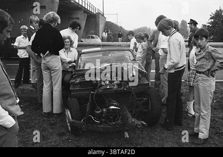 Car accident, Whizgle News, Dutch Desk, The Netherlands, 1950 - 2000 on 27-09-1970. The image shows these topics. In a scene bustling with activity, a group of individuals gathers around a damaged vehicle, which prominently occupies the foreground. The car, an older model, is missing its front end, exposing its engine and giving it a rugged, distressed appearance. Surrounding the vehicle, a diverse crowd of onlookers showcases various styles of clothing typical of the era, with some individuals in light-colored, casual attire and others sporting more formal looks. A mix of adults and children Stock Photo