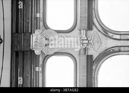 Restored railway carriage + hr. Karskens Treinen, Whizgle News, Dutch Desk, The Netherlands, 1950 - 2000 on 12-04-1977. These topics are shown in the image. The scene centers on an intricately designed door handle, emphasizing a vintage or antique aesthetic. The handle is metallic and features ornate engravings, highlighting craftsmanship and attention to detail. It is positioned centrally, drawing the eye towards its elegant shape and embellishments. The door itself appears to be made of rich, dark wood, showcasing a polished finish that reflects light subtly, enhancing its depth and texture. Stock Photo