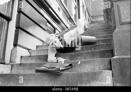 Series of unemployed people: going out - working in the garden - carpentry - falling down the stairs - rowing with the oars - wheelbarrow - pushing over a wall - taking the big step - civil servant Unemployed unemployment, Whizgle News, Dutch Desk, The Netherlands, 1950 - 2000 on 16-10-1982. These topics appear in the image. The scene depicts a whimsical moment captured on a set of stone steps. A person is sprawled forward, seemingly clinging to the edge of the steps, with an exaggerated expression that conveys a mix of surprise and determination. The individual is dressed in a white shirt and Stock Photo