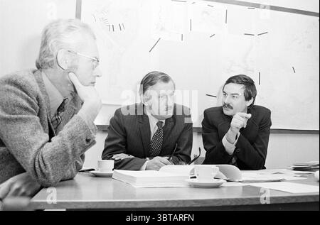 Engineers from Rijkswaterstaat for Port Plan Ports, Whizgle News, Dutch Desk, The Netherlands, 1950 - 2000 on 05-02-1976. The image contains these topics. In a well-lit conference room, three men are seated around a large table, deeply engaged in discussion. The men are dressed in suits, suggesting a formal business setting. Two of them have graying hair, while the third has a darker, slicked-back hairstyle. Their expressions convey concentration, with furrowed brows and attentive gazes focused on the matter at hand. The table is cluttered with papers and documents, some stacked neatly while o Stock Photo