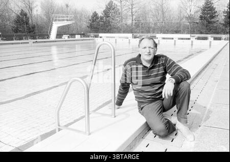 Swimming pool staff, Whizgle News, Dutch Desk, The Netherlands, 1950 - 2000 on 04-1988. The image shows these topics. In a tranquil outdoor setting, a man is seated by the edge of a swimming pool. The pool is large, featuring clear water that reflects the soft light of the day, creating a serene atmosphere. The tiles lining the pool have a subtle pattern, enhancing the geometric alignment of the space. The man, wearing a striped black and gray long-sleeve shirt and light-colored pants, rests comfortably on one knee, with his other leg extended and positioned on the ground. His casual pose and Stock Photo