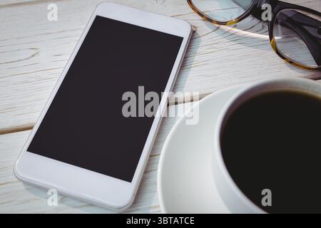 Flat design smartphone showing blank screen is lying on tabletop with coffee cup and glasses nearby Stock Photo