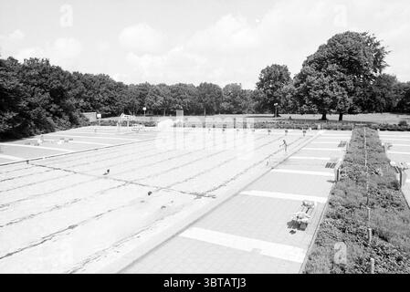 Empty swimming pool Heerenduinen, Whizgle News, Dutch Desk, The Netherlands, 1950 - 2000 on 24-07-1993. The image shows these topics. The scene depicts a spacious outdoor swimming pool area, captured in shades of black and white, emphasizing contrasts between light and shadow. The pool is divided into several lanes, with clear, reflective water shimmering under a bright sky. Surrounding the pool, the concrete deck is uniformly laid out, featuring a grid-like pattern that adds to the symmetry of the composition. To one side, there are a few benches, their simple designs highlighting a minimalis Stock Photo