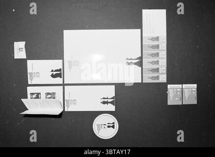 HST exhibition Moriaan Blast Furnace Chess Tournament Wijk aan Zee, Whizgle News, Dutch Desk, The Netherlands, 1950 - 2000 on 19-01-1981. The image includes these topics. The scene presents an organized arrangement of various items on a dark surface, creating a striking contrast against the background. At the center, a large, blank white sheet is positioned, serving as a focal point. Surrounding it are several smaller items, predominantly made of white and muted colors, including cards and envelopes, which display silhouettes in a monochromatic scheme. The cards vary slightly in size and featu Stock Photo
