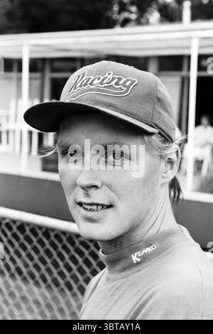 Baseball player Benno Maat RCH Heemstede Heemstede The Netherlands, Whizgle News, Dutch Desk, The Netherlands, 1950 - 2000 on 23-07-1997. The image includes these topics. A young man stands prominently in the foreground, showcasing a subtle yet confident expression. His light blonde hair is neatly combed back and his fair complexion is accentuated by the contrast of the dark cap he wears, emblazoned with the word 'Racing' in a bold, script font. The cap’s color is a rich shade of blue that complements the muted tones of his clothing, which appears to be a fitted gray garment. In the background Stock Photo