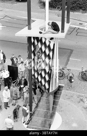 Fire brigade artwork Haarlem The Netherlands, Whizgle News, Dutch Desk, The Netherlands, 1950 - 2000 on 07-05-1993. The image includes these topics. The scene captures a bustling urban environment, centered around a striking architectural structure. The structure itself is modern and abstract, featuring a series of intersecting lines and geometric shapes, with a prominent tall pole and a large platform at its peak. Below, a crowd of individuals is gathered, exhibiting a mix of curiosity and engagement. They are dressed in casual attire, with a variety of styles indicating different ages and ba Stock Photo