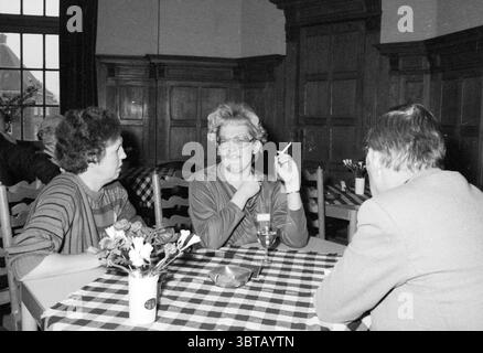 Working visit of the Queen's Commissioner Zandvoort Zandvoort Zandvoort, Whizgle News, Dutch Desk, The Netherlands, 1950 - 2000 on 21-03-1985. These are the topics in the image. The scene reveals a lively indoor gathering. Three individuals are seated at a table adorned with a checked tablecloth, featuring a pattern of alternating white and dark squares. The ambiance feels both relaxed and intimate, indicative of a social meeting. On one side of the table, two women engage in conversation. The first woman has curly dark hair and wears a textured pattern on her top, projecting a casual yet thou Stock Photo