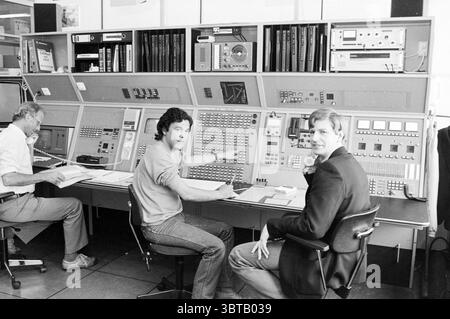 Men Lin Haring technical control room R.L.D. [National Aviation Service] Schiphol, Whizgle News, Dutch Desk, The Netherlands, 1950 - 2000 on 13-05-1985. The image shows these topics. In a retro-futuristic control room, a large console dominated the center, sprawling across the width of the scene. The console featured numerous buttons, knobs, and screens, exhibiting an array of dials and illuminated indicators. The color palette included muted gray tones, accented by flashes of green, red, and orange lights emanating from various controls, creating a slightly industrial atmosphere. To the left, Stock Photo