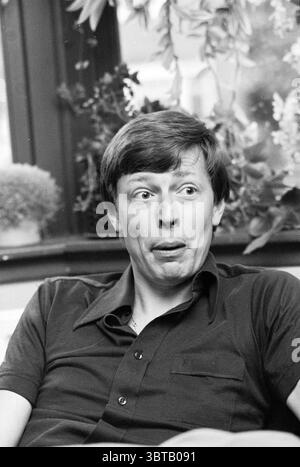 Portrait Paul Captijn D'66 Politics people politics, Whizgle News, Dutch Desk, The Netherlands, 1950 - 2000 on 19-05-1978. The image shows these topics. A man is seated comfortably, facing slightly towards his left. He has short hair with a casual style and wears a dark-colored, short-sleeved, collared shirt. His expression conveys surprise or amusement, with his eyes wide and mouth slightly open as if caught mid-laugh or making a funny expression. The setting appears warm and inviting, illuminated by soft, natural light that floods through a large window behind him. This window, framed by dar Stock Photo
