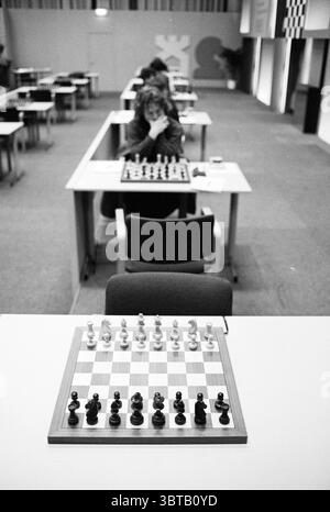 HST decathlon [Boogovens Chess Tournament], Whizgle News, Dutch Desk, The Netherlands, 1950 - 2000 on 19-01-1995. The image contains these topics. The scene captures a setting arranged for a chess tournament, characterized by a minimalistic and structured layout. In the foreground, a polished wooden chess board is prominently displayed, featuring alternating light and dark squares. The pieces are arranged neatly, ready for play, with a clear distinction between the black and white sets, which adds a sense of order. In the mid-ground, several tables are lined up in a neat row, each equipped wit Stock Photo