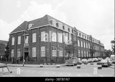 Ext. HTS Verspronckweg Exterior Haarlem Verspronckweg The Netherlands, Whizgle News, Dutch Desk, The Netherlands, 1950 - 2000 on 28-08-1969. These topics are shown in the image. The scene presents a large, brick building characterized by its rectangular form and a pitched roof adorned with tiles. The architecture is clearly functional, reflecting a classic, institutional style common in mid-20th century constructions. Rows of windows line the facade, their frames painted white, offering a striking contrast against the darker bricks. Surrounding the building, a neatly maintained urban environme Stock Photo