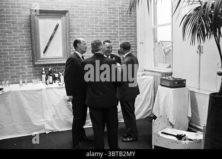 Frydal Techniek N.V. Amsterdam Opening openings commissioning, Whizgle News, Dutch Desk, The Netherlands, 1950 - 2000 on 12-10-1962. These topics are shown in the image. In a warmly lit indoor space, four men are engaged in conversation, their expressions animated and lively. They are dressed in formal attire, with dark suits that contrast against the neutral tones of the room. The setting features exposed brick walls, adding texture and warmth to the environment. A white tablecloth-draped surface is filled with an assortment of wine bottles, glasses, and some partially empty decanters, sugges Stock Photo