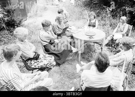 Heimanshof native garden reading Hoofddorp Hoofddorp The Netherlands, Whizgle News, Dutch Desk, The Netherlands, 1950 - 2000 on 31-07-1992. The image shows these topics. In a relaxed outdoor setting, a group of individuals is gathered around a circular table surrounded by lush greenery. The scene conveys a sense of community and conversation, with several people seated on colorful chairs positioned around the table. The colors are predominantly muted, with shades of gray and black conveying a classic, timeless quality. Each person displays a unique style through their clothing, ranging from pa Stock Photo