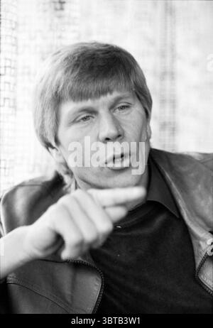 Portrait of Martin van Vianen trainer Telstar Telstar Football, Whizgle News, Dutch Desk, The Netherlands, 1950 - 2000 on 12-12-1979. The image shows these topics. In a warm, softly lit indoor setting, a man is seated, engaged in animated conversation. His hair is light and styled in a neat manner, and he has a pronounced expression that suggests he is making a significant point. His lips are pursed, and his brow is slightly furrowed, emphasizing his earnestness. He is dressed in a dark top, likely black, layered beneath a leather jacket that has a textured, deep brown hue. His body language i Stock Photo