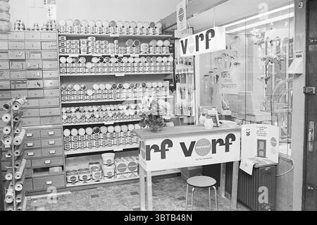 Interior hardware store Spaarnwouderstraat. Interior Haarlem Spaarnwouderstraat The Netherlands, Whizgle News, Dutch Desk, The Netherlands, 1950 - 2000 on 16-01-1970. These are the elements in the image. The scene depicts a vintage retail space, likely a hardware or craft store. The interior is filled with shelves lined with various containers of paint, each in different sizes and colors, predominantly neutral tones like whites, beiges, and muted pastels. The containers are neatly organized, creating a visually appealing pattern against the background. To one side, a wooden counter stands prom Stock Photo