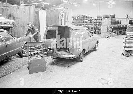 Velsen Animal Protection Ambulance in garage., Whizgle News, Dutch Desk, The Netherlands, 1950 - 2000. The image contains these topics. The scene captures a bustling garage environment filled with various items and activities. On the left, a man is engaged with a vintage car, working near its front. He appears focused, possibly examining or repairing something under the hood. His attire suggests a mechanic's role, complete with rugged work clothes. In the foreground, an old, partially dismantled car door leans against a wall, indicating ongoing work and creating a sense of disarray. Near the d Stock Photo