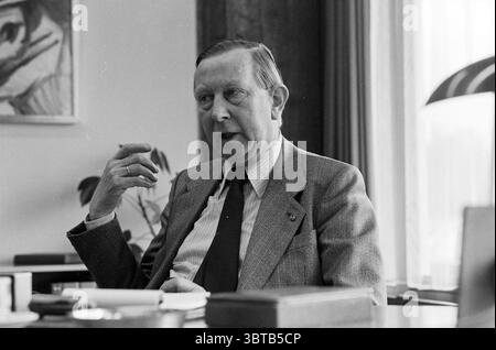 Mr. Haagsma Tax Office Haarlem Persons Haarlem The Netherlands, Whizgle News, Dutch Desk, The Netherlands, 1950 - 2000 on 09-11-1981. These topics are shown in the image. In a well-lit office space, a middle-aged man occupies the foreground. He is seated at a desk, dressed in a tailored, light-colored suit that contrasts subtly with his dark tie. His posture is relaxed yet attentive, with one hand raised as he gestures, suggesting engagement in conversation or thought. The background features a wall adorned with an abstract artwork, which adds a touch of creativity to the professional setting. Stock Photo