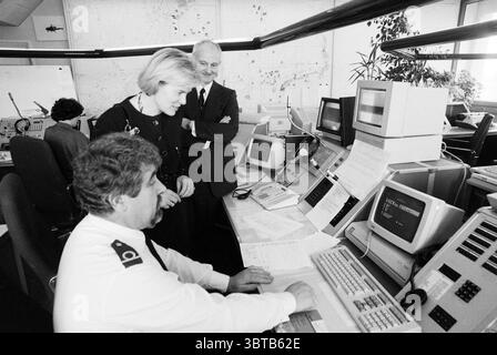 May Weggen at radio Scheveningen, Whizgle News, Dutch Desk, The Netherlands, 1950 - 2000 on 31-03-1992. The image contains these topics. In a bustling office environment filled with vintage technology, various individuals are engaged in what appears to be a collaborative effort. The space is characterized by tall desks adorned with multiple computer monitors, some displaying pixelated screens typical of earlier computing eras, while papers and documents are strewn about, hinting at an organized chaos. The color palette is primarily monochrome, dominated by shades of gray which evoke a professi Stock Photo