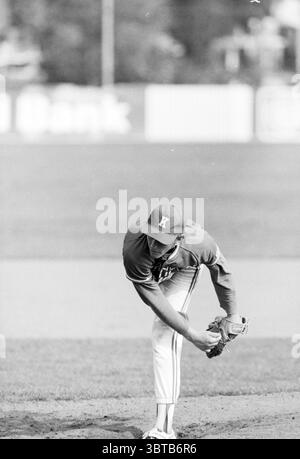 Baseball Ksn@@e@@ - KCAW, Whizgle News, Dutch Desk, The Netherlands, 1950 - 2000 on 26-08-1990. These topics are shown in the image. The scene captures a baseball player on the pitcher's mound, poised in a focused stance. Clad in a uniform adorned with a prominent letter on the cap, the player’s body is slightly bent forward, balancing on one leg while the other knee is raised. The colors of the uniform are a mix of light and dark shades, creating a striking contrast with the natural earth tones of the playing field. Surrounding the player, the baseball diamond is visible, marked by rich green Stock Photo