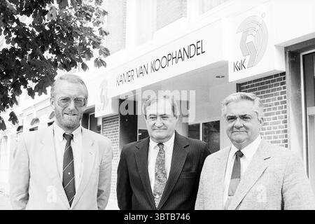 Delegation of the American Chamber of Commerce opens the trade chamber at the Haarlem Chamber of Commerce Haarlem The Netherlands, Whizgle News, Dutch Desk, The Netherlands, 1950 - 2000 on 01-08-1989. The image contains these topics. Three individuals stand together in front of a building featuring large windows and a prominent sign above. The exterior of the structure is predominantly light-colored bricks, suggesting a modern architectural style. The first person on the left has gray hair and wears glasses, dressed in a light-colored suit with a tie, exuding a professional demeanor. To his ri Stock Photo