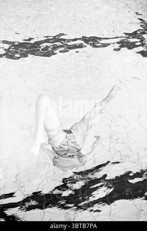 Professional swimmers in the pool, Whizgle News, Dutch Desk, The Netherlands, 1950 - 2000 on 09-07-1988. The image shows these topics. The scene captures an under-the-water perspective within a swimming pool. The water is clear, with light reflections creating a play of shimmering patterns on the surface. The focus is on a figure submerged, partially obscured by the rippling water. The person wears a bikini, with the distinctive lines of the swimsuit appearing slightly distorted due to the water's surface tension. Their legs are visible, one bent at the knee while the other is extended, sugges Stock Photo