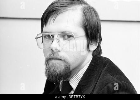 Mr Masselink of Rijkswaterstaat Persons Prov. States Prov. Water Management Provincial House, Whizgle News, Dutch Desk, The Netherlands, 1950 - 2000 on 15-10-1981. These are the elements in the image. The scene features a young man with a serious expression. His hair is dark and slightly tousled, falling around his forehead. He has a prominent beard that is neatly trimmed, adding to his thoughtful demeanor. Large, round eyeglasses frame his face, enhancing the intensity of his gaze as he looks directly at the viewer. He is dressed in a dark, textured blazer that contrasts with a light-colored, Stock Photo