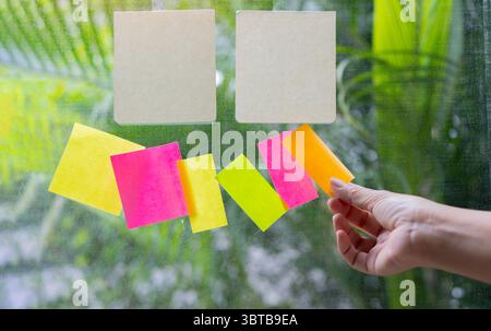 Close-up people holding paper post it in hand on glass wall board. Empty space for text. Stock Photo