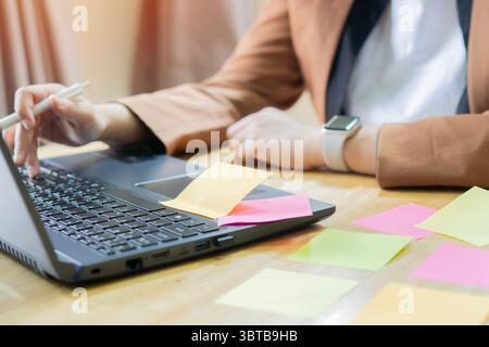 Young Asian businesswoman brainstorming strategy and new ideas on laptop with adhesive notes. Selective focus. Stock Photo