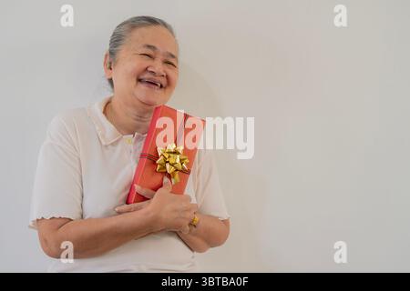 Christmas, Asian senior and happy woman with gift in portrait at studio for holiday celebration over white background with copy space. Stock Photo