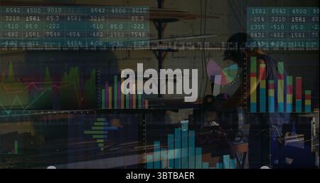 Operating welder in apron grinding pipe on bench in metal shop, with data charts, copy space Stock Photo